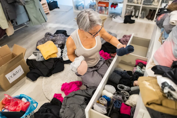 Older woman sorting clothes into boxes while decluttering a closet before downsizing