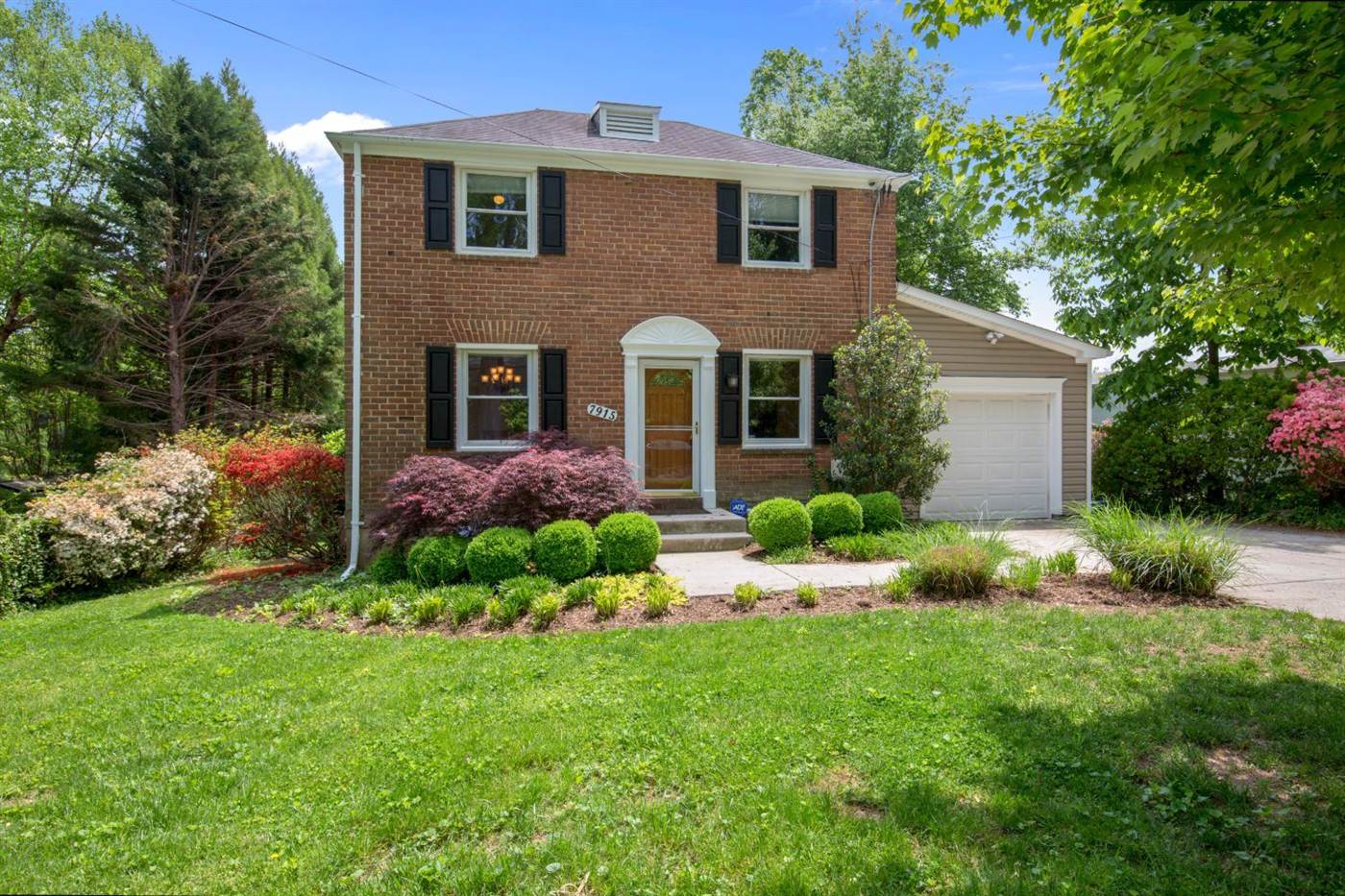 Brick colonial home with black shutters and azaleas in bloom