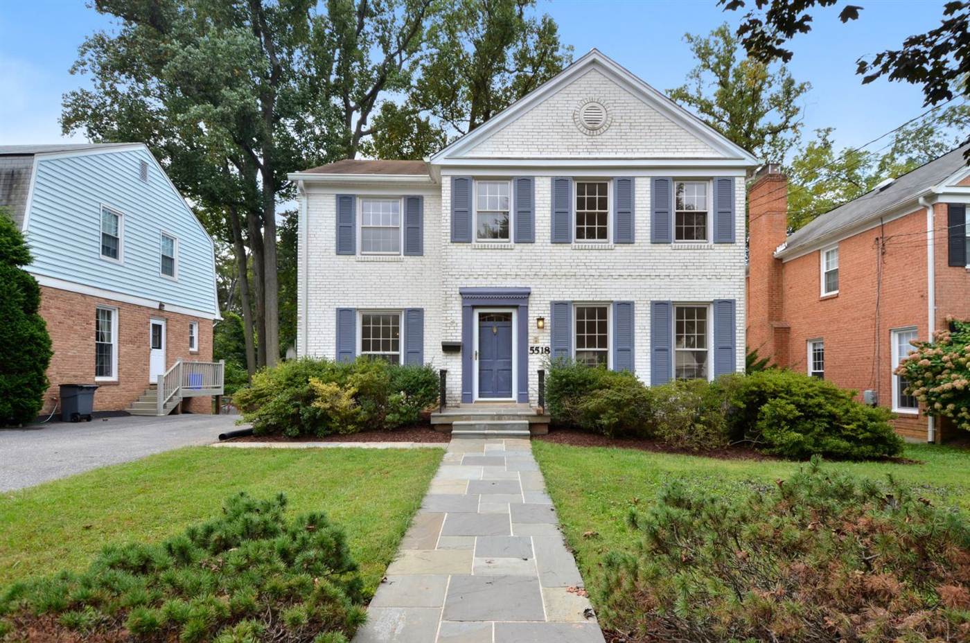 White brick colonial home with blue shutters and a stone walkway