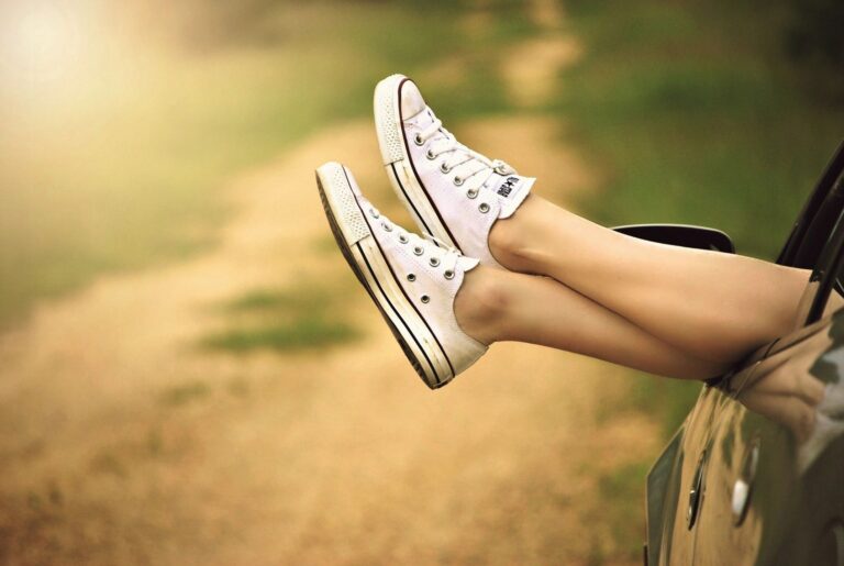 Feet in white sneakers resting out a car window on a summer road trip