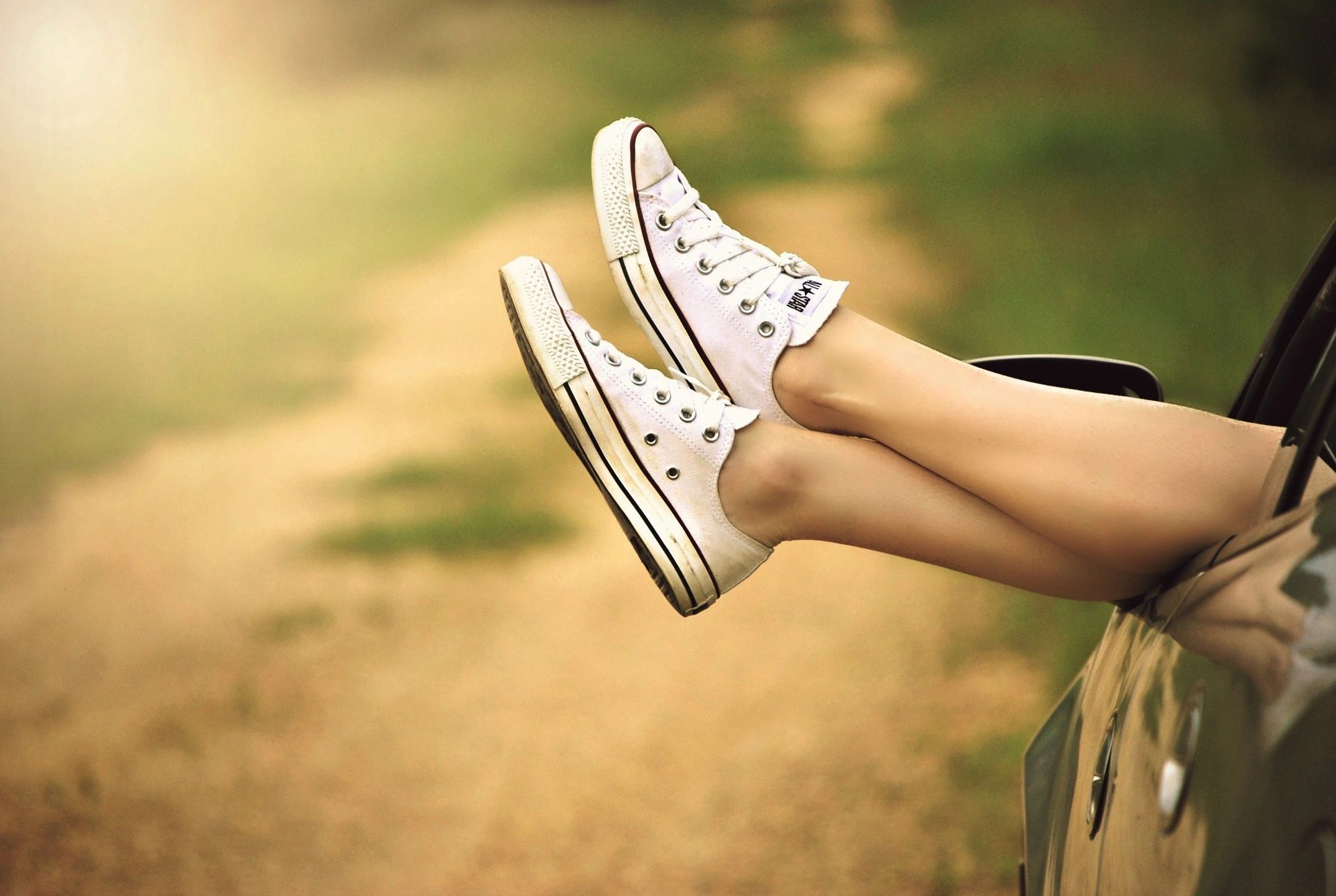 Feet in white sneakers resting out a car window on a summer road trip