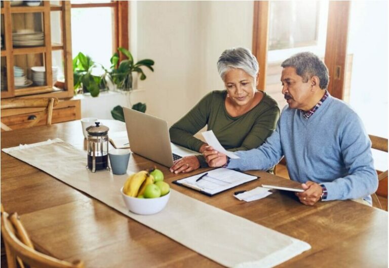 Senior couple reviewing property tax paperwork together at a kitchen table with a laptop